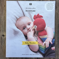 A crocheted Baby Blankies pattern book with Ricorumi branding, on a wood background