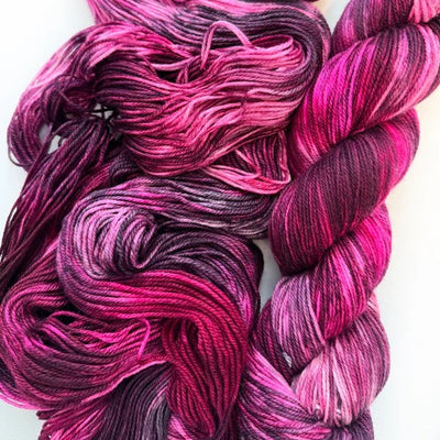 Hot pink and dark purple yarn skeins and loose yarn on a white background