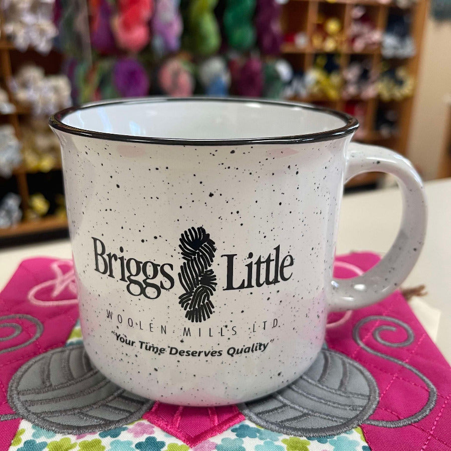 Speckled mug with 'Briggs Little' logo on a colorful quilted surface