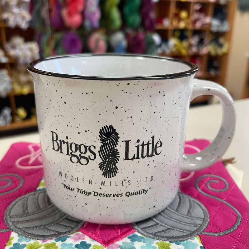 Speckled mug with 'Briggs Little' logo on a colorful quilted surface
