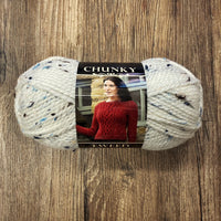 Ball of white yarn with blue and black tweed flecks with a Chunky Tweed label on a wood background