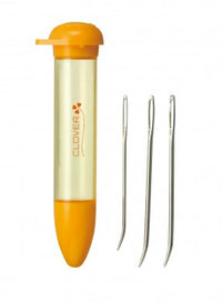 An orange and clear plastic needle tube with a screw-top lid, shown next to three metal bent-tip wool needles on a plain white background. The tube features the Clover brand logo.