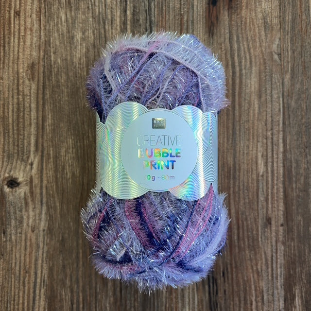 Ball of purple and pink variegated scrubby yarn with white label on a wood background