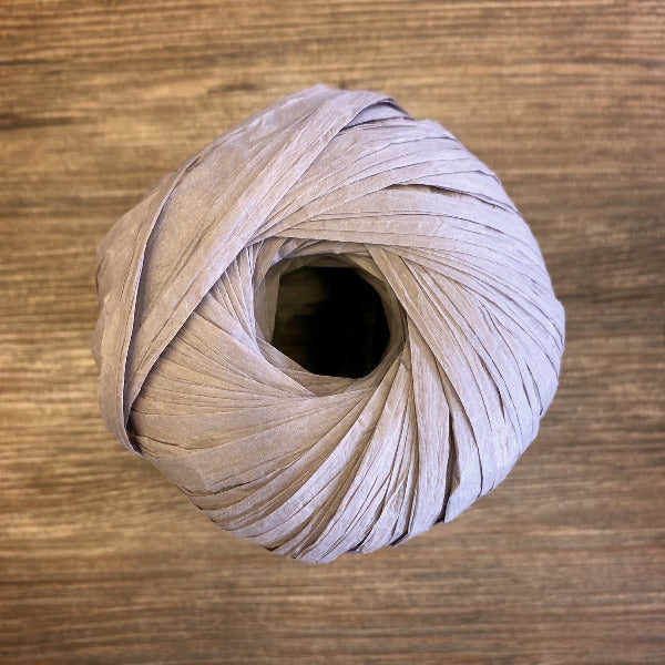 A ball of taupe paper yarn on a wood background
