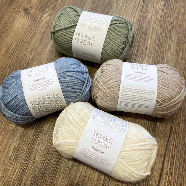 Four skeins of yarn in green, blue, beige, and white on a wooden surface with 'Double Sunday' labels.