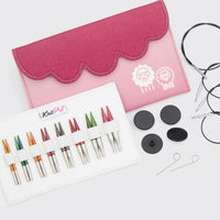 Knitting needle set with colorful needles, accessories, and a pink case on a white background.