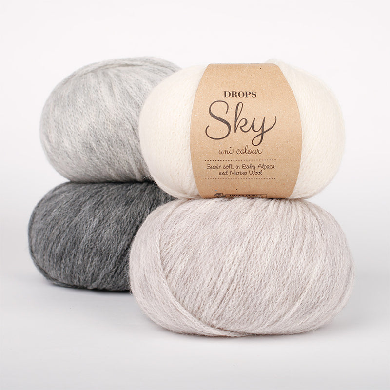 Four balls of yarn in greys, white, and beige with a label on a white background