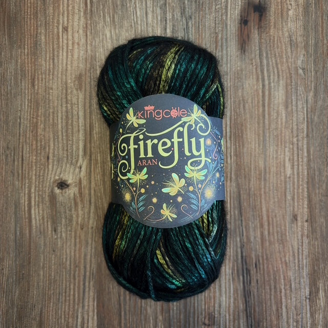 A ball of King Cole Firefly Aran yarn, featuring dark green, black, and gold variegated yarn, resting on a rustic wooden surface.