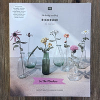 A crocheted flowers pattern book with Ricorumi branding, on a wood background
