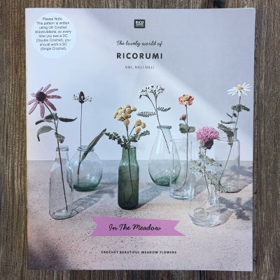 A crocheted flowers pattern book with Ricorumi branding, on a wood background