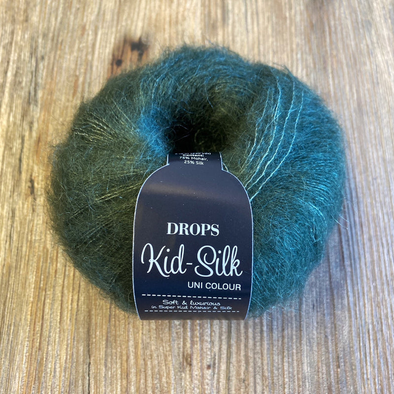 Ball of green yarn with a 'DROPS Kid-Silk' label on a wooden surface