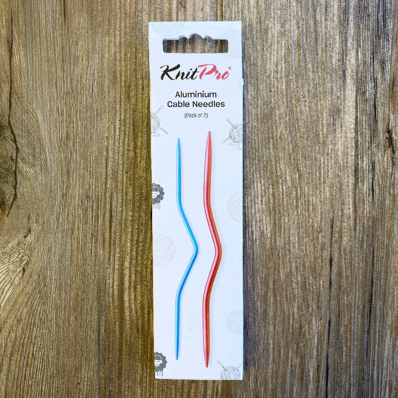 White KnitPro box with 2 sizes of cable needles on it, on a wood background