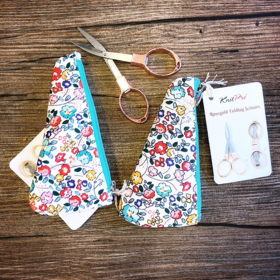 Floral-patterned scissors case with a pair of folding scissors on a wooden surface