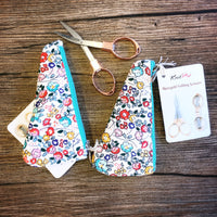 Floral-patterned scissors case with a pair of folding scissors on a wooden surface
