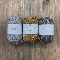Three metallic balls of yarn with labels on a wood background