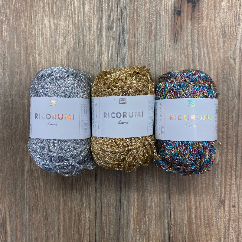 Three metallic balls of yarn with labels on a wood background