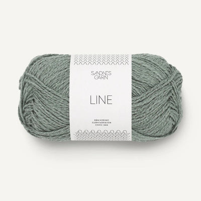 Ball of sage green yarn with a label on a white background