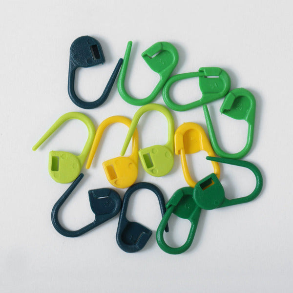 Set of green, yellow, and dark green plastic safety pins on a white background