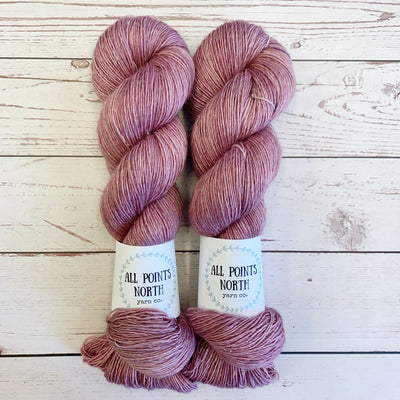 Two skeins of pink yarn with All Points North labels on a white wood background