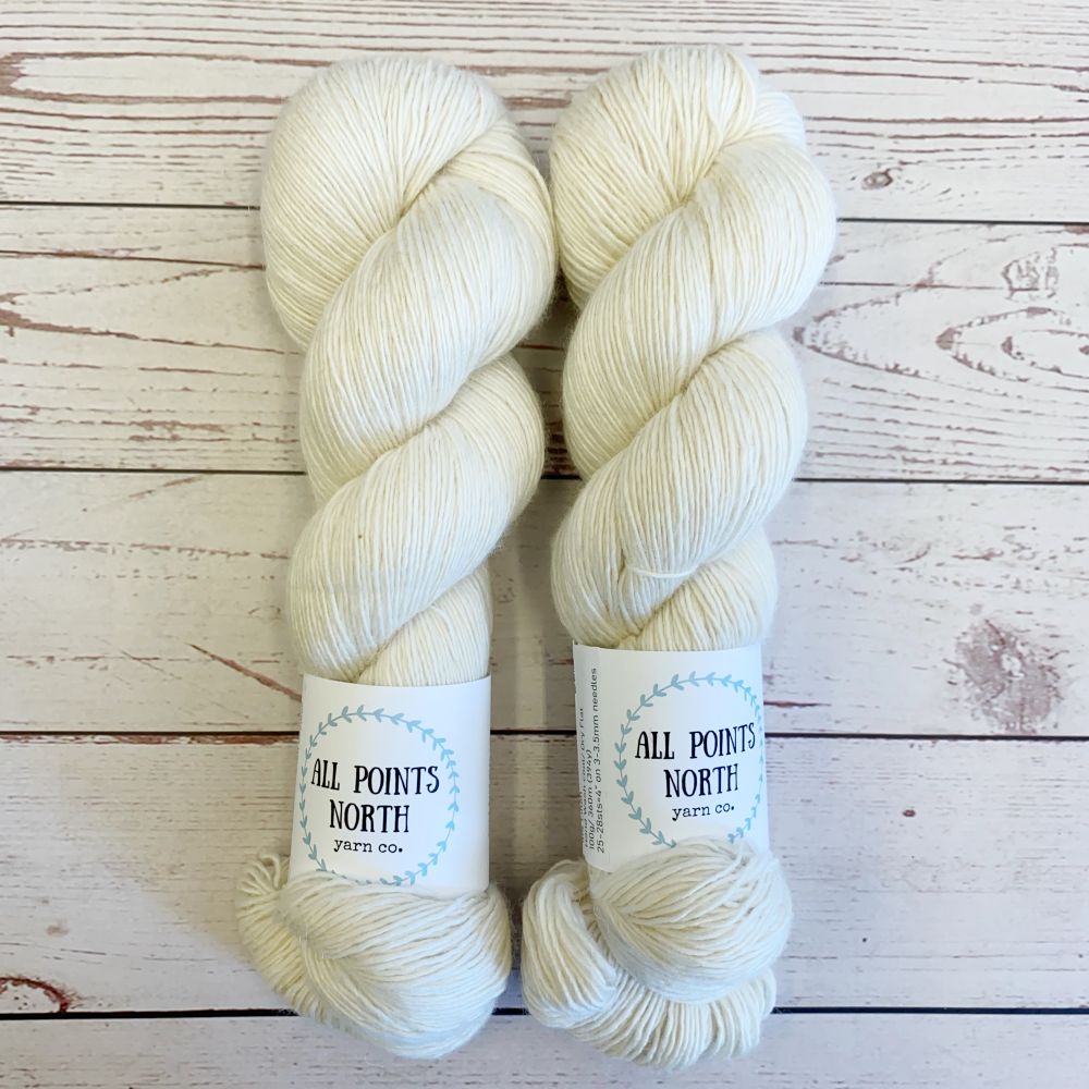 Two skeins of cream yarn with All Points North labels on a white wood background