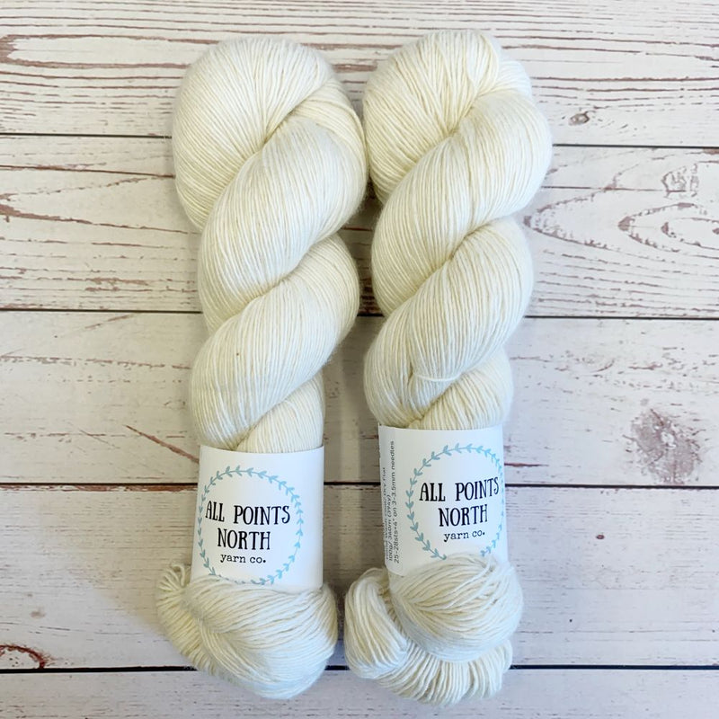 Two skeins of cream yarn with All Points North labels on a white wood background