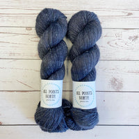 Two skeins of charcoal coloured yarn with All Points North labels on a white wood background
