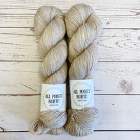 Two skeins of beige yarn with All Points North labels on a white wood background