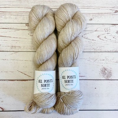 Two skeins of beige yarn with All Points North labels on a white wood background