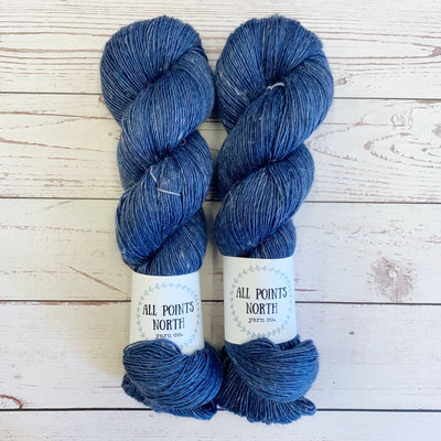 Two skeins of blue yarn with All Points North labels on a white wood background