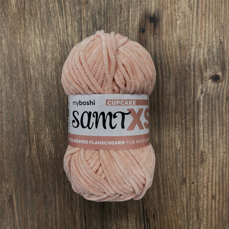 Ball of pink yarn with a label on a wooden surface