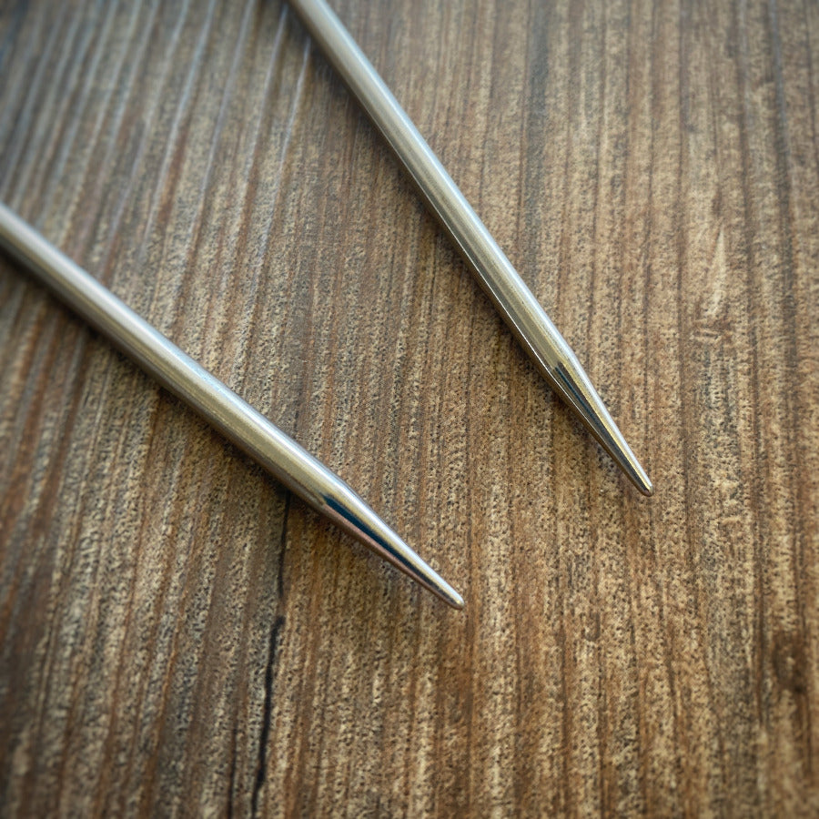 Close up of two metal needle tips on a wooden surface