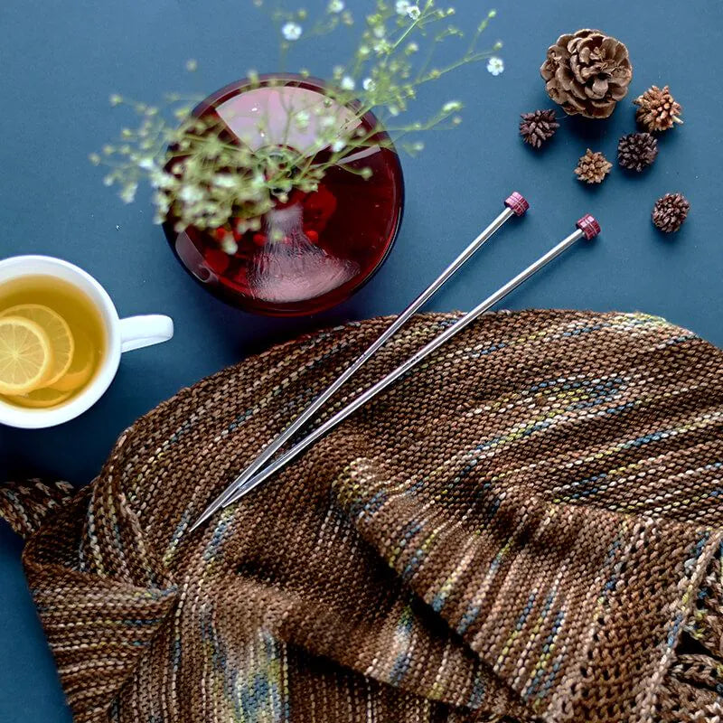 Knitting needles on a knitted fabric with a cup of tea and decorative items on a blue background