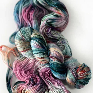 Multicolored skeins and loose yarn in pinks and teals on a white background