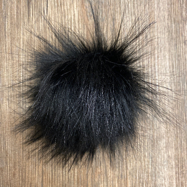 Black fluffy pom-pom on a wooden surface