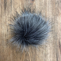 Dark grey and white fluffy faux fur pom-pom om a wooden surface