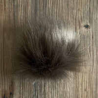 Grey-brown coloured fluffy faux fur pom-pom on a wooden surface