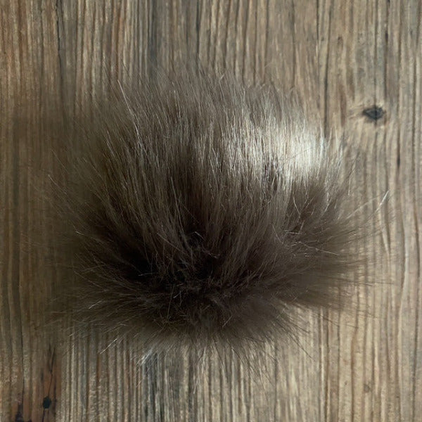 Grey-brown coloured fluffy faux fur pom-pom on a wooden surface