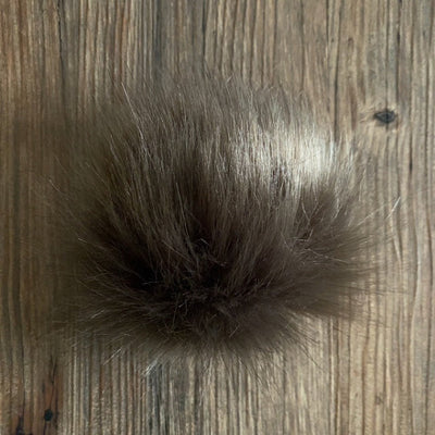 Grey-brown coloured fluffy faux fur pom-pom on a wooden surface