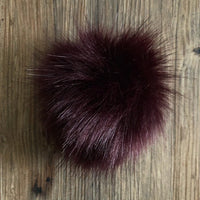 Deep wine coloured faux fur pom-pom on a wooden surface