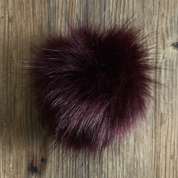 Deep wine coloured faux fur pom-pom on a wooden surface