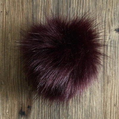 Deep wine coloured faux fur pom-pom on a wooden surface