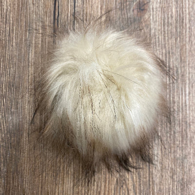 Beige and tan fur pom-pom on a wooden surface