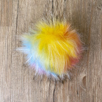 Yellow, blue, pink, and white fluffy pom-pom on a wooden surface