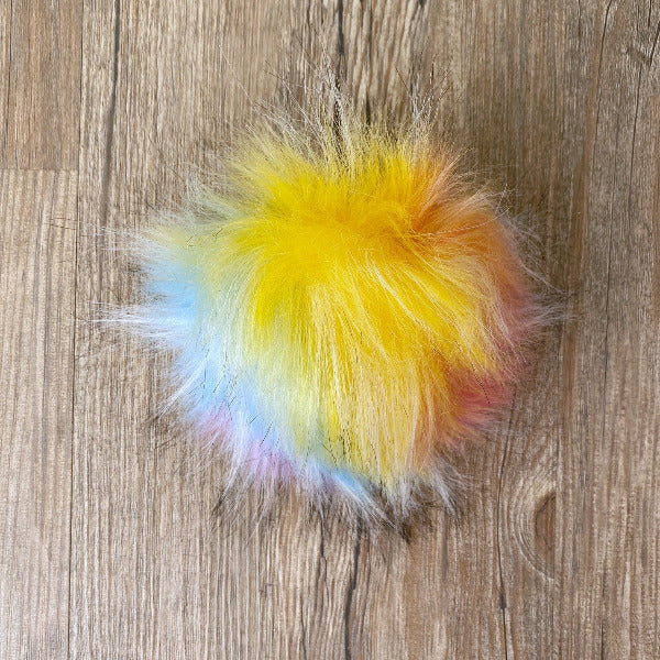 Yellow, blue, pink, and white fluffy pom-pom on a wooden surface