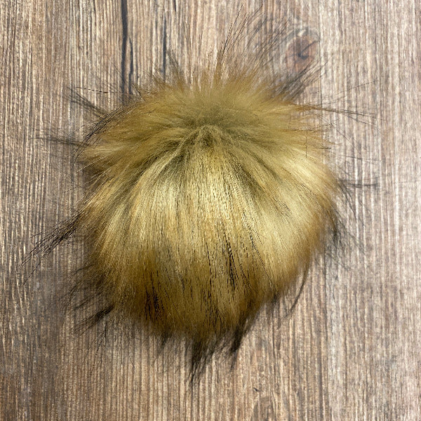 Yellow/brown faux fur pom-pom on a wooden surface