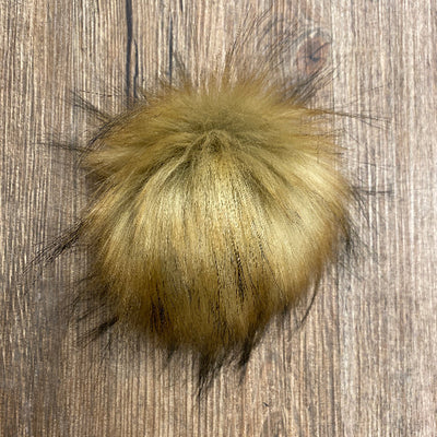Yellow/brown faux fur pom-pom on a wooden surface