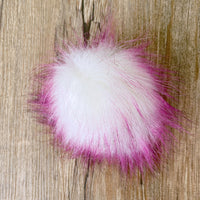 White and pink fluffy pom-pom on a wooden surface