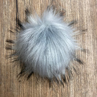 Gray fluffy pom-pom on a wooden surface