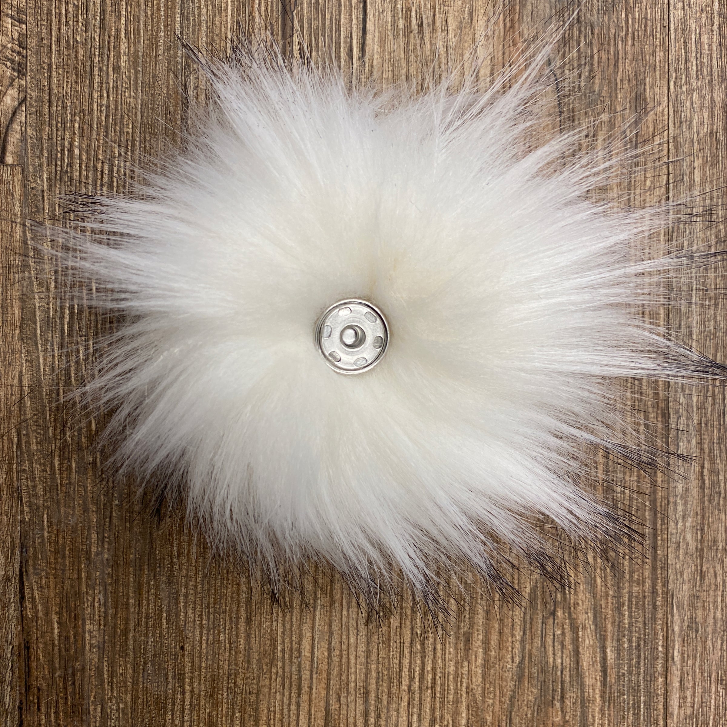 White fluffy pom-pom with a central snap button on a wooden surface