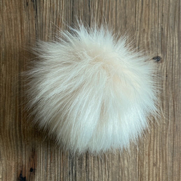 Cream fluffy pom-pom on a wooden surface